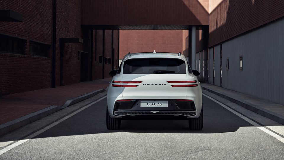 Rear view of a white regular GV70 in a brick-lined street.