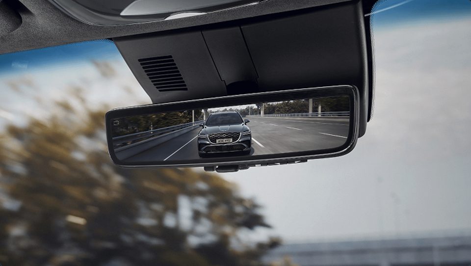 Interior center mirror showing a camera view of the road and a following vehicle.